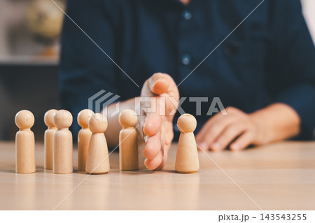 Hand separates one wooden figure from a group, representing workforce restructuring, employee separation, team division, selection, organizational change, staffing decisions, and HR management. 143543255