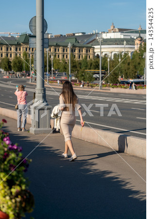 Woman Walking on Urban Bridge in Summer Light With City Buildings and Flowers in Background Woman Walking on Urban Bridge in Summer Light With City Buildings and Flowers in Background 143544235