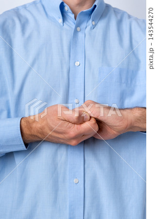 Man's hands clasped tightly together in front of his torso, wearing a light blue dress shirt, conveying concepts of focus, patience, anticipation, or contemplation in a professional setting Man's hands clasped tightly together in front of his torso, wearing a light blue dress shirt, conveying concepts of focus, patience, anticipation, or contemplation in a professional setting 143544270