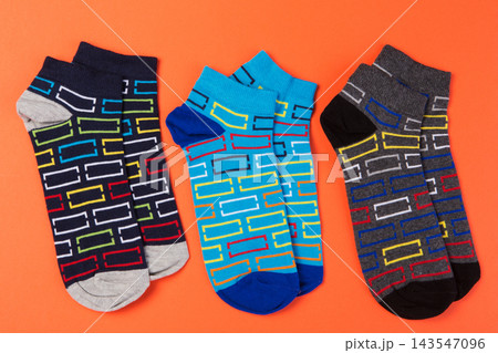 Three pairs of colorful low cut socks with geometric pattern arranged on bright orange background Three pairs of colorful low cut socks with geometric pattern arranged on bright orange background 143547096