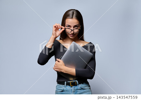 Confident young woman adjusting glasses and holding a laptop 143547559