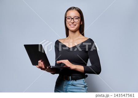 Young woman in glasses holding laptop and looking at camera in studio Young woman in glasses holding laptop and looking at camera in studio 143547561
