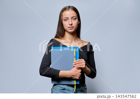 Young female student holding notebook in studio portrait Young female student holding notebook in studio portrait 143547562