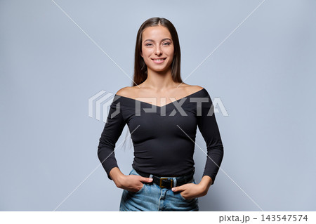 Portrait of a smiling young woman in a black top and jeans on a gray background Portrait of a smiling young woman in a black top and jeans on a gray background 143547574
