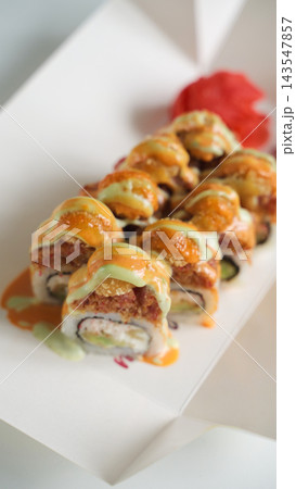 Sushi rolls with spicy tempura topping and avocado filling in a white takeout box, with red pickled ginger Sushi rolls with spicy tempura topping and avocado filling in a white takeout box, with red pickled ginger 143547857