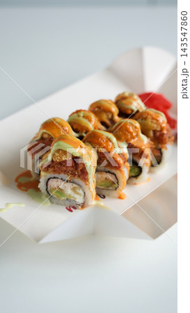 Spicy fried salmon maki rolls with avocado and cream cheese, topped with sauce and ginger, in a takeaway box 143547860
