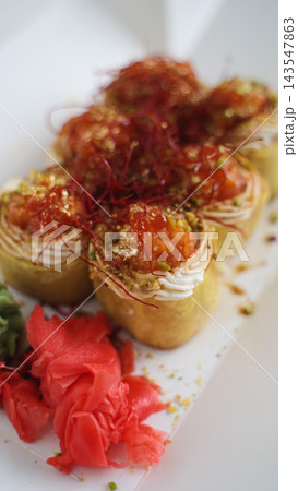 Gourmet salmon sushi rolls with cream cheese, chili threads, pistachios, and gold flakes, served with pickled ginger Gourmet salmon sushi rolls with cream cheese, chili threads, pistachios, and gold flakes, served with pickled ginger 143547863