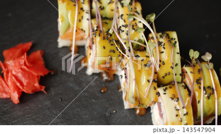 Uramaki sushi rolls with salmon, avocado, black sesame seeds, and sauce, served with ginger on a slate plate Uramaki sushi rolls with salmon, avocado, black sesame seeds, and sauce, served with ginger on a slate plate 143547904
