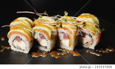 Uramaki sushi rolls on a dark background, chef adding sauce and microgreens, gourmet Japanese food 143547906