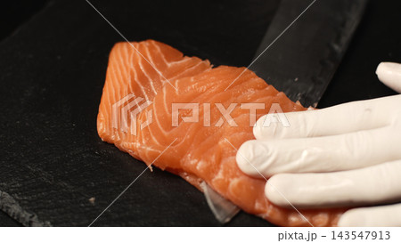 Chef's gloved hands slicing fresh raw salmon fillet for seafood preparation and healthy cooking Chef's gloved hands slicing fresh raw salmon fillet for seafood preparation and healthy cooking 143547913