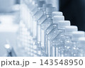 Close up of a row of PET bottles moving on a conveyor belt in a light blue scene 143548950