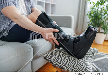 Person resting leg in orthopedic boot on ottoman at home Person resting leg in orthopedic boot on ottoman at home 143549116