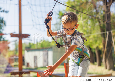 Boy navigating ropes course outdoors with safety harness Boy navigating ropes course outdoors with safety harness 143549632