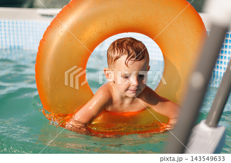 Young boy swimming with inflatable ring in outdoor pool 143549633