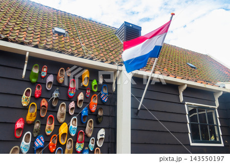 National flag of the Netherlands waving on a traditional wooden house wall decorated with colorful clogs under a tiled roof in Zaanse Schans, Netherlands National flag of the Netherlands waving on a traditional wooden house wall decorated with colorful clogs under a tiled roof in Zaanse Schans, Netherlands 143550197