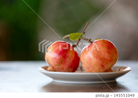 Two fresh ripe pomegranates on a plate on wooden table with soft bokeh background 143551049