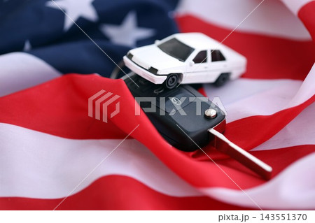 Ignition keys with remote control buttons and toy car on United States flag. Car driving in USA Ignition keys with remote control buttons and toy car on United States flag. Car driving in USA 143551370