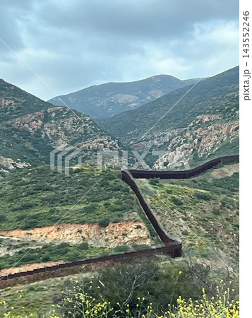 メキシコ・バハカリフォルニア州の険しい緑の山岳地帯をジグザグに這うアメリカとの国境の壁の景観 メキシコ・バハカリフォルニア州の険しい緑の山岳地帯をジグザグに這うアメリカとの国境の壁の景観 143552246