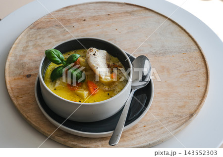 Belgian Waterzooi in a Dark Bowl on a Wooden Board. Belgian waterzooi fish soup in a dark bowl on a white saucer and wooden board seen from above, a creamy broth with white fish, potato and carrot fin Belgian Waterzooi in a Dark Bowl on a Wooden Board. Belgian waterzooi fish soup in a dark bowl on a white saucer and wooden board seen from above, a creamy broth with white fish, potato and carrot fin 143552303