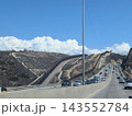 メキシコ・ティフアナの国境沿い高速道路を走る車列と丘陵にそびえ立つアメリカとの国境の壁のインフラ景観 143552784