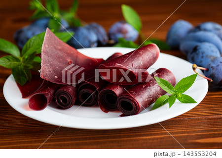 Homemade plum fruit leather rolls with fresh plums on wooden table Homemade plum fruit leather rolls with fresh plums on wooden table 143553204
