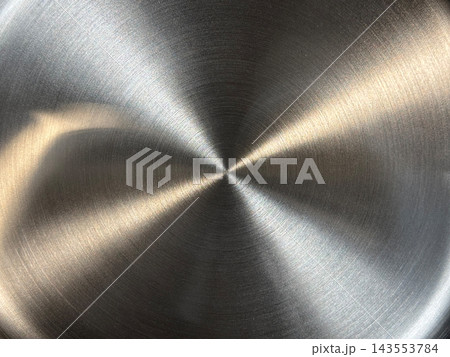 Close-up of circular brushed stainless steel with fine concentric grain and a bowtie-shaped pattern of warm golden highlights and dark sectors 143553784