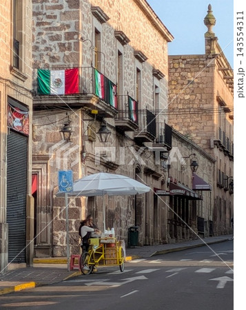 世界遺産メキシコ・モレリアの歴史地区に佇む移動式カートの屋台と国旗が掲げられた伝統の石造り建築 143554311