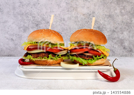 Two double cheeseburgers with fresh lettuce, tomato, cream cheese, chili peppers, bacon, onion, and a patty on a wooden tray, food delivery concept, menu and advertising for cafes and restaurants 143554886