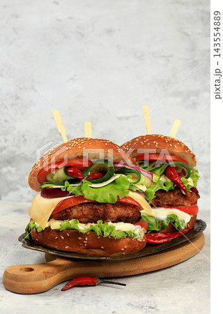 Two double cheeseburgers with fresh lettuce, tomato, cream cheese, cucumber, onion, chili pepper and a patty on an old wooden board,food delivery concept,menu and advertising for cafes and restaurants Two double cheeseburgers with fresh lettuce, tomato, cream cheese, cucumber, onion, chili pepper and a patty on an old wooden board,food delivery concept,menu and advertising for cafes and restaurants 143554889