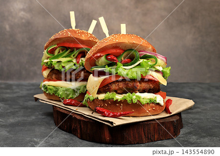Two double cheeseburgers with fresh lettuce, tomato, cream cheese, cucumber, onion, chili pepper and a patty on an old wooden board,food delivery concept,menu and advertising for cafes and restaurants 143554890