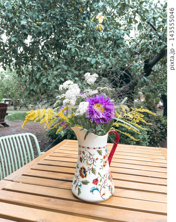 Wildflower bouquet in ceramic pitcher on wooden table in garden Wildflower bouquet in ceramic pitcher on wooden table in garden 143555046