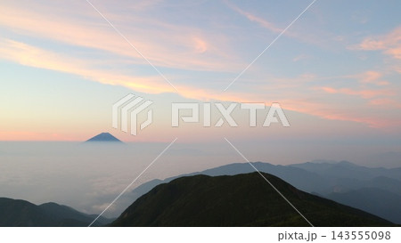 ピンク色の朝焼け雲と、雲海の向こうに浮かぶ円すい形の山 143555098
