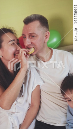 Husband eating a chip from his wife's hand. Playful love, trust and family humor. Husband eating a chip from his wife's hand. Playful love, trust and family humor. 143556941