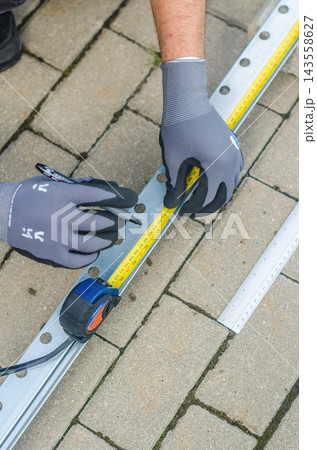 Overhead view of gloved hands using tape measure and pen to mark metal channel rail on pavement, construction measuring.. High quality photo Overhead view of gloved hands using tape measure and pen to mark metal channel rail on pavement, construction measuring.. High quality photo 143558627