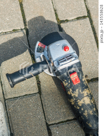 Close-up of worn angle grinder with cutting disc resting on paving stones, used power tool with visible wear and dirt.. High quality photo 143558628