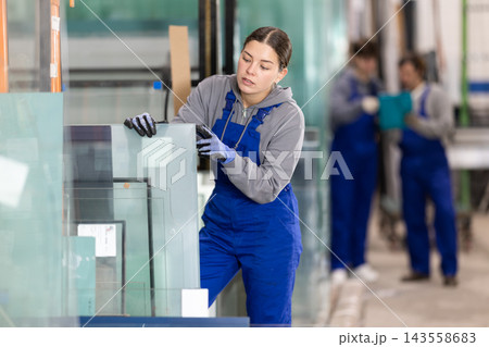 Girl glazer employee in blue overall works in glass processing shop 143558683