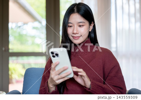 Young Asian woman checking smartphone on sofa in a living room or cafe 143559309
