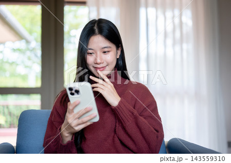 Young Asian woman looking at smartphone on sofa in a living room or cafe Young Asian woman looking at smartphone on sofa in a living room or cafe 143559310