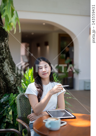 Asian Woman with Tablet and Coffee Gesturing with Stylus Outdoors Asian Woman with Tablet and Coffee Gesturing with Stylus Outdoors 143559431