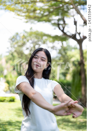 Asian Woman Stretching Arms and Warming Up Outdoors in Park 143559442