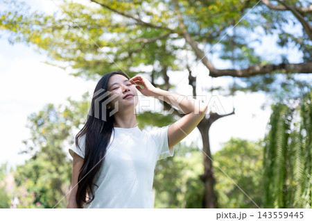Asian Woman Touching Hair Enjoying Warm Sunlight Outdoors in Park Asian Woman Touching Hair Enjoying Warm Sunlight Outdoors in Park 143559445