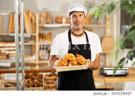 Middle-aged salesman displaying croissants in square wicker basket Middle-aged salesman displaying croissants in square wicker basket 143559487