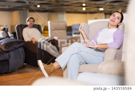 Man and woman sitting around in armchairs in furniture store Man and woman sitting around in armchairs in furniture store 143559584