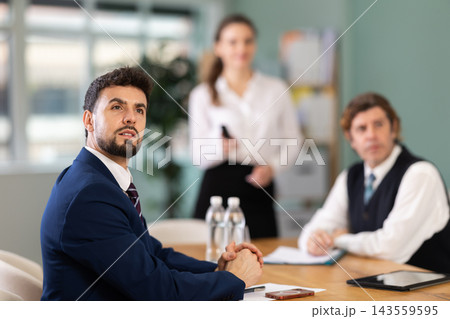 Business partners sitting at table and chatting, colleague with remote control telling at background 143559595