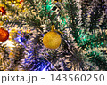Close up of golden bauble ornament on Christmas tree decorated with silver tinsel garland 143560250