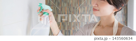 自宅の浴室で笑顔で洗剤をスプレーしながら拭き掃除をする日本人女性の横顔顔無しバナー 143560634