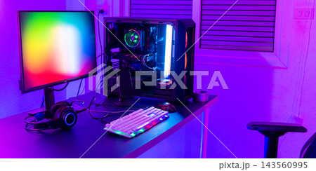 A computer setup with a purple light dark background, games transmission modern equipment, modern gaming PC on desk with keyboard mouse monitor A computer setup with a purple light dark background, games transmission modern equipment, modern gaming PC on desk with keyboard mouse monitor 143560995