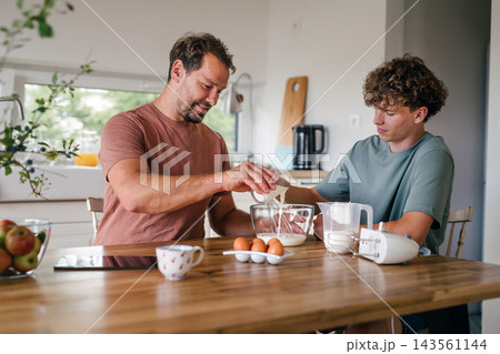 Father and teenage son baking homemade cake in kitchen. 143561144