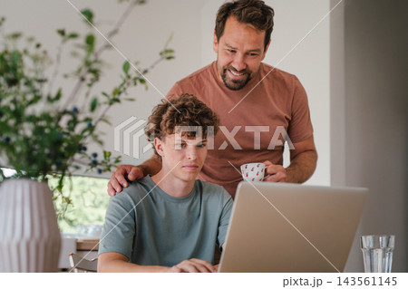 Father supporting teenage son checking university admission decision online. Father supporting teenage son checking university admission decision online. 143561145