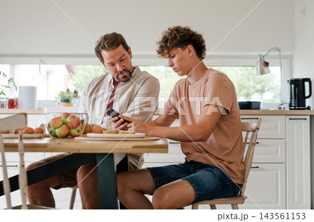 Father and teenage son having breakfast together, looking at phone. Father and teenage son having breakfast together, looking at phone. 143561153